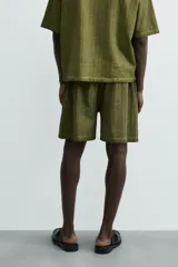 Bermuda de algodón color verde oliva, con corte relajado y textura acanalada vertical. Presenta cintura elástica con cordón interior y bolsillos laterales y trasero.