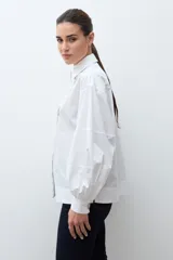 Camisa blanca de corte recto con cuello clásico, cierre frontal de botones y mangas largas con puños abullonados.