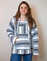 Buzo estilo mexicano con capucha, tejido en hilo grueso a rayas horizontales blancas y negras, con bolsillo tipo canguro y cordones ajustables en el cuello.
