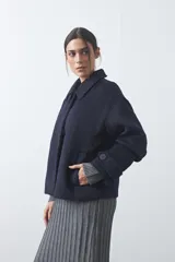 Tapado corto de paño con textura, color marrón, de corte recto y silueta estructurada. Presenta cuello camisero, cierre frontal con botones grandes y mangas largas con detalle de trabas en los puños.
