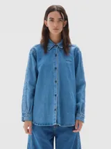 Camisa de denim soft con lavado stone wash, manga larga, cuello clásico y cierre frontal con botones. Presenta un bordado con la palabra 'PASTICHE' en el pecho.