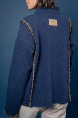 Buzo de lana color beige con cuello redondo y mangas largas. Presenta costuras decorativas con bordado en color naranja a lo largo de los costados y en los puños.