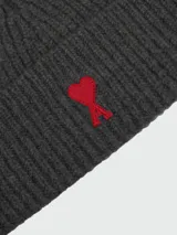 Gorro tipo beanie de punto acanalado en color gris oscuro, con el logo de corazón característico de Ami Paris bordado en rojo en la parte frontal.