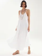 Vestido largo blanco de breteles finos, corte holgado y escote redondo. Incluye dos collares de cuentas y sandalias bajas con tiras.
