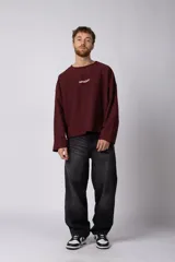 Buzo de cuello redondo confeccionado en tejido rústico con bordes al corte y costuras expuestas. Presenta un diseño boxy con estampado frontal y es reversible, permitiendo su uso por ambos lados.