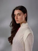 Saco largo de punto color blanco, confeccionado en 100% lana merino natural, con diseño jacquard de ramas, cuello alto, cierre frontal con pequeños botones y aberturas laterales.