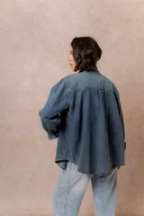 Camisa de denim de lavado medio con calce oversize, cuello camisero, cierre frontal con botones y bolsillos aplicados en el frente.