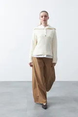 Sweater de tejido de punto color blanco, con cuello polo, cierre frontal con botones metalizados y mangas largas levemente acampanadas. Presenta un corte relajado con pequeñas aberturas laterales en el ruedo.