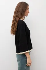 Sweater de punto negro con escote bote, mangas largas y detalles de terminación en ondas de color blanco en el cuello, los puños y el ruedo.