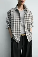Camisa relaxed fit confeccionada en tejido de mezcla de algodón con textura irregular, diseño a cuadros en tonos gris, marrón y blanco, con cuello solapa, manga larga con puño abotonado, bolsillo de parche en el pecho y cierre frontal con botones.