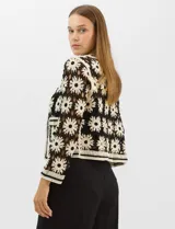 Cardigan abierto de tejido crochet con diseño de flores bicolores en negro y crema. Presenta mangas largas, frente abierto sin cierre y bolsillos frontales tipo parche. Posee terminaciones con franjas a contraste en escote, puños y ruedo.