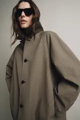 Trench reversible de corte recto con cuello de solapa y aplicación de pelo sintético extraíble. Presenta cierre frontal con botones, manga larga y bolsillos laterales ocultos en las costuras.