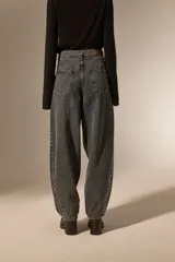 Pantalon de jean estilo barrel con lavado oscuro, tiro medio y detalle de tachas metálicas a lo largo de las costuras laterales.