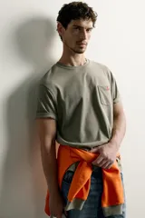 Camiseta verde militar de corte regular, con cuello redondo, manga corta y un bolsillo de parche en el pecho con etiqueta decorativa contrastante.