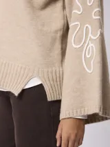 Sweater de tejido de punto color beige, con cuello redondo, mangas largas acampanadas y diseño bordado en color blanco en las mangas.