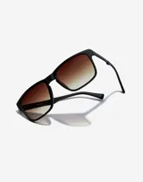 Lentes de sol Hawkers Peak Metal unisex, con montura cuadrada negra y lentes degradadas de marrón a transparente.