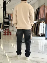 Buzo de felpa color beige con medio cierre frontal y cuello alto. Presenta estampado frontal con texto en contraste y diseño de estilo urbano.