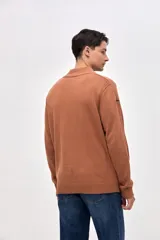 Buzo de punto color azul, con cuello alto y cierre frontal parcial. Presenta un diseño con textura acanalada en los hombros y mangas, y un pequeño bordado en la manga derecha.