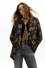 Chaqueta de corte sastre confeccionada en tejido jacquard con diseño floral en tonos dorados y azules sobre base negra. Presenta doble botonadura con botones metálicos en color bronce, bolsillos plaqué frontales, mangas largas y tajo en la espalda.