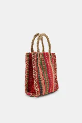 Mini bolso cuadrado de yute 100%, con diseño de rayas multicolor en tonos rojos, verdes y tostados. Cuenta con asas de mano rígidas forradas en yute y costuras decorativas entrelazadas en los laterales.