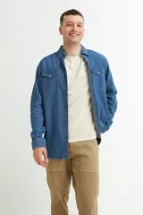 Camisa de denim azul con cuello clásico, cierre frontal con botones a presión, dos bolsillos con solapa abotonada en el pecho y mangas largas con puños abotonados.