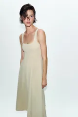 Vestido midi de color beige con escote cuadrado y tirantes anchos. Presenta un diseño entallado en el torso con costuras verticales marcadas y una falda con caída evasé.