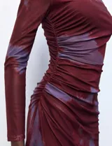 Vestido midi de microtul con diseño drapeado lateral, cuello alto y mangas largas. Presenta un estampado tipo tie-dye en tonos bordó y violeta.