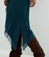 Pollera midi de satén color verde petróleo, con corte asimétrico y detalle de encaje aplicado en el ruedo. Presenta una cintura estructurada y una caída fluida.