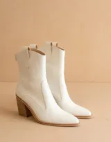 Bota texana de caña media color blanco, con taco cuadrado de madera y punta ligeramente afinada. Presenta un diseño minimalista con cierre posterior y tiradores laterales.