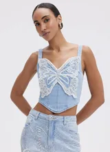 Top tipo corsé de denim celeste, estructurado con varillas internas, tirantes anchos y bajo en punta. Presenta un aplique frontal en forma de mariposa bordado a mano con cuentas y lentejuelas plateadas y blancas.