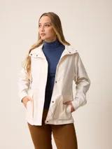 Campera de corte recto y estilo funcional, color beige, con capucha integrada, cierre frontal con botones a presión y bolsillos delanteros amplios. Presenta un diseño minimalista con cordones ajustables en la capucha.