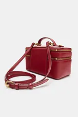 Bolso tipo vanity color tostado con pespuntes en contraste. Cuenta con asa de mano superior, doble compartimento con cierre de cremallera y correa bandolera ajustable y extraíble.