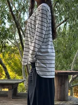 Remerón de manga larga, color blanco con rayas horizontales negras, corte oversize con tajos laterales y bajo redondeado.