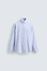 Camisa de algodón de corte regular, color celeste claro con finas rayas blancas verticales. Presenta cuello abotonado (button-down), manga larga con puños abotonados y un bolsillo plastrón en el pecho izquierdo.