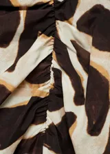 Falda midi de viscosa con estampado animal print en tonos marrones y crema. Presenta un diseño recto con detalle drapeado lateral y una abertura pronunciada en la pierna. Cuenta con cierre de cremallera invisible en la parte posterior.