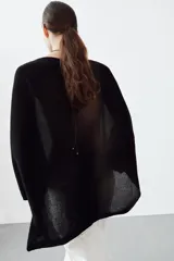 Jersey de punto con diseño tipo capa asimétrica, cuello redondo y mangas largas con puños ajustados.