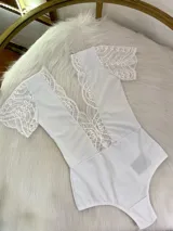 Body de color blanco con escote profundo en V, confeccionado en lycra opaca con detalles de encaje y microtul en el frente y las mangas cortas.