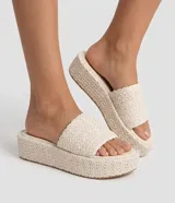 Sandalia flatform Satinato color beige, con suela plana y plataforma alta forrada en material sintético trenzado. Cuenta con una tira ancha superior con textura trenzada y puntera redonda.