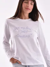 Remera de manga larga color crema con cuello redondo y un estampado central de un ramo de flores rosadas y naranjas en un jarrón azul oscuro.