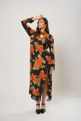 Vestido largo negro con estampado de flores naranjas y amarillas, cuello mao con abertura en forma de gota, mangas largas acampanadas con botones en los puños, tajo lateral y flecos en el ruedo.