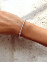 Pulsera rígida tipo brazalete con estructura de resorte, decorada con múltiples charms de metal plateado, cuentas de vidrio con motivos florales y geométricos, y dijes colgantes incluyendo un corazón con inscripción y un dije de árbol de la vida.