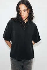Camisa de manga corta color marrón oscuro, con cuello solapa, cierre frontal oculto con botones y dos bolsillos de parche en el pecho.