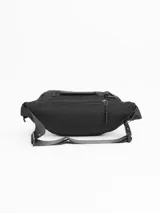 Riñonera urbana de diseño funcional en color negro. Cuenta con dos compartimentos frontales con cierre, un bolsillo trasero oculto de seguridad, manija superior de transporte y correa ajustable con cierre de broche. Incluye parche con logo de la marca en el frente.
