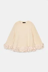 Jersey de punto color crema con cuello redondo y mangas tres cuartos. Presenta un diseño holgado con el ruedo decorado con aplicaciones de flores de tela en relieve.