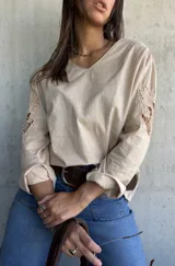 Blusa color beige con escote en V, manga larga y detalles de encaje calado en los hombros.