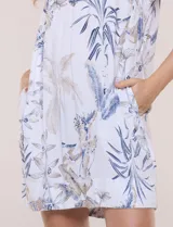 Vestido corto marca Dash confeccionado en mezcla de lino y rayón, color blanco con estampado botánico en tonos azules y beige. Presenta escote en V con cuello tipo camisa, mangas cortas, bolsillos laterales invisibles y una silueta holgada de caída ligera.
