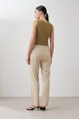 Pantalón de corte recto y tiro medio, confeccionado en tela de gabardina color beige. Presenta cierre frontal con cremallera y botón oculto, bolsillos laterales y costuras verticales decorativas en la parte superior.