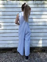 Mono largo de corte holgado con diseño de rayas verticales finas en azul y blanco. Presenta breteles anchos para atar sobre los hombros y piernas de corte ancho tipo palazzo.