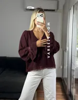 Blusa de tela cey color bordó, con escote en V y mangas largas abullonadas que terminan en puños con detalle de encaje y volados.