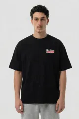 Remera negra de corte estándar con estampa gráfica colorida en la espalda que presenta un personaje con cabeza amarilla, rodeado de elementos abstractos y el texto 'Vernal Club'.
